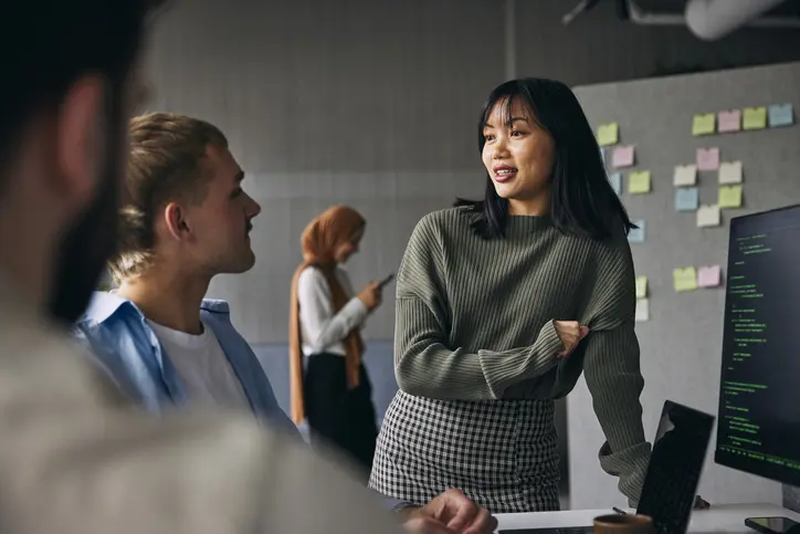 A woman converses with a man in a modern office setting, both engaged in a professional discussion.
